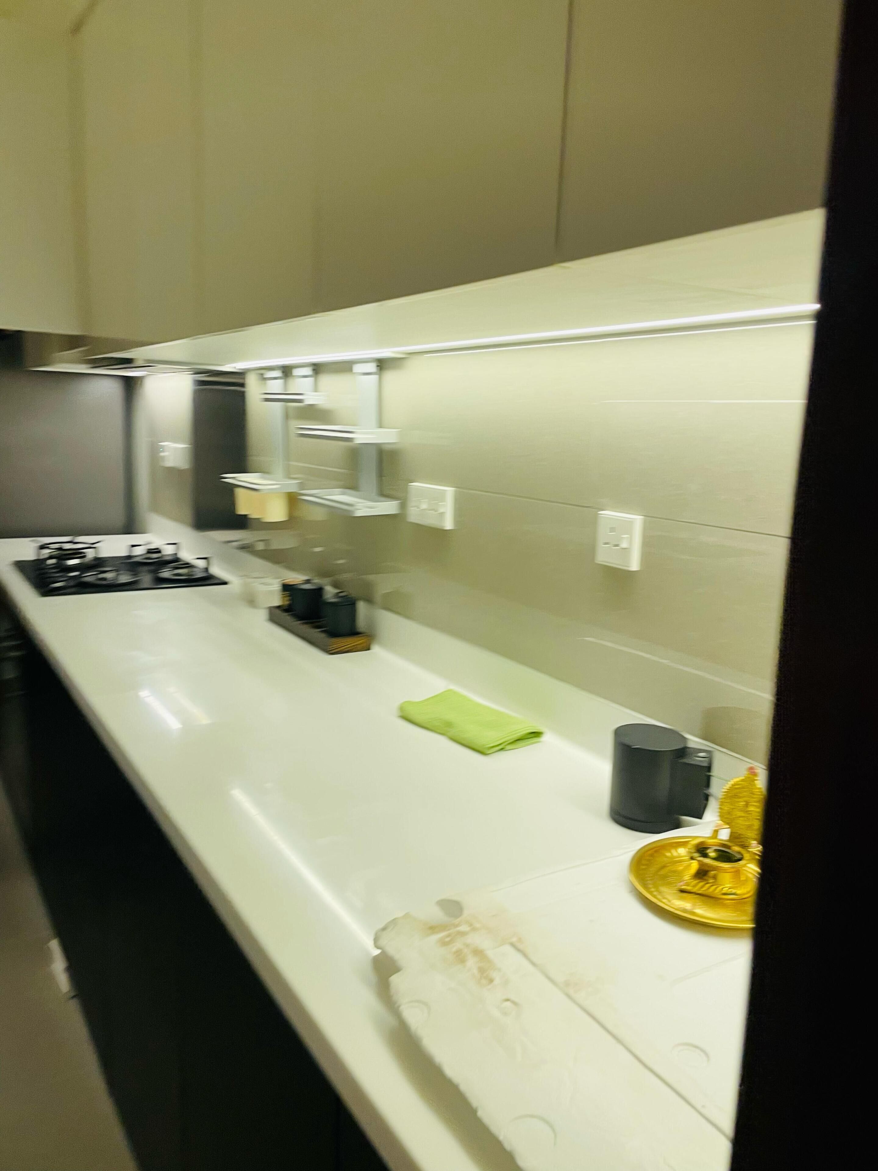 A kitchen with a white countertop, a stove, a coffee maker, and a small trash bin.