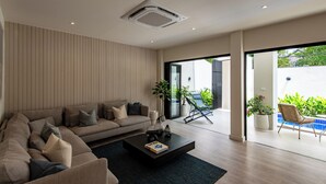 A modern living room with a sofa, a coffee table, and a view of a balcony with plants. - Palazzo 126 • Luxury 5BR Pool Villa in Patong (Patong, Kathu)