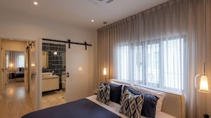 A modern hotel room with a large bed, a bathroom with a bathtub, and a view of the city through large windows. - Palazzo 126 • Luxury 5BR Pool Villa in Patong (Patong, Kathu)