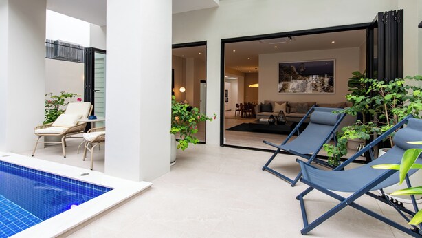 A modern indoor pool area with lounge chairs, a small seating area with chairs, and a large window. - Palazzo 126 • Luxury 5BR Pool Villa in Patong (Patong, Kathu)