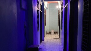 A narrow hallway with a tiled floor, blue lighting, and a ceiling with recessed lighting. - Hotel Krishna Inn (Karchana)