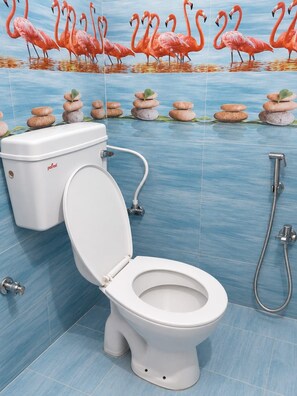 Une salle de bain comprenant des toilettes, un bidet et un mur décoré d’un motif de flamant rose et d’éléments en pierre.