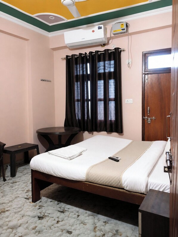 Une chambre d’hôtel équipée d’un lit, d’un bureau, d’une chaise, d’un climatiseur et d’une fenêtre avec des rideaux.