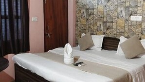 A bedroom with a bed, a ceiling fan, an air conditioning unit, a window with a metal grill, and a patterned wall. - Hotel Krishna Inn (Karchana)