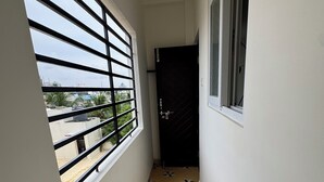 A narrow corridor with a window on the left and a door at the end. The floor has a geometric tile pattern.