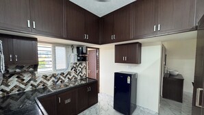 A kitchen with dark wooden cabinets, a black refrigerator, and a tiled backsplash.