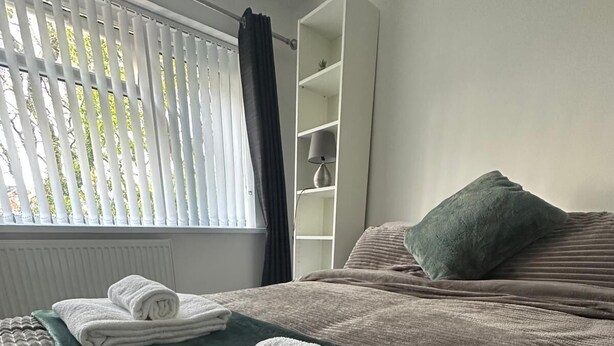 Ein ordentlich gemachtes Bett mit einer grünen Decke und zwei aufgerollten weißen Handtüchern.
