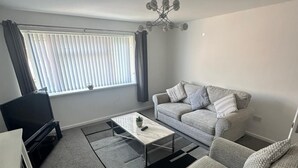 Ein modernes Wohnzimmer mit einem grauen Sofa, einem Couchtisch und einem Fernseher.