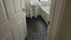 Ein kleines Badezimmer mit einem weißen Waschbecken, einem Fenster und einem schwarz-weißen Fliesenboden.