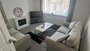 Ein Wohnzimmer mit einer Couch, einem Couchtisch, einem Fernseher und einer dekorativen Uhr.