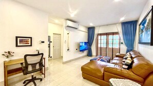 Uma sala de estar com sofá, televisão, escrivaninha e uma cadeira.