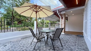 Um alpendre coberto com uma mesa redonda e cadeiras, um grande guarda-sol e vista para o verde.