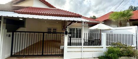 Una casa residencial con entrada protegida por una reja, un patio cubierto y un techo de tejas rojas.