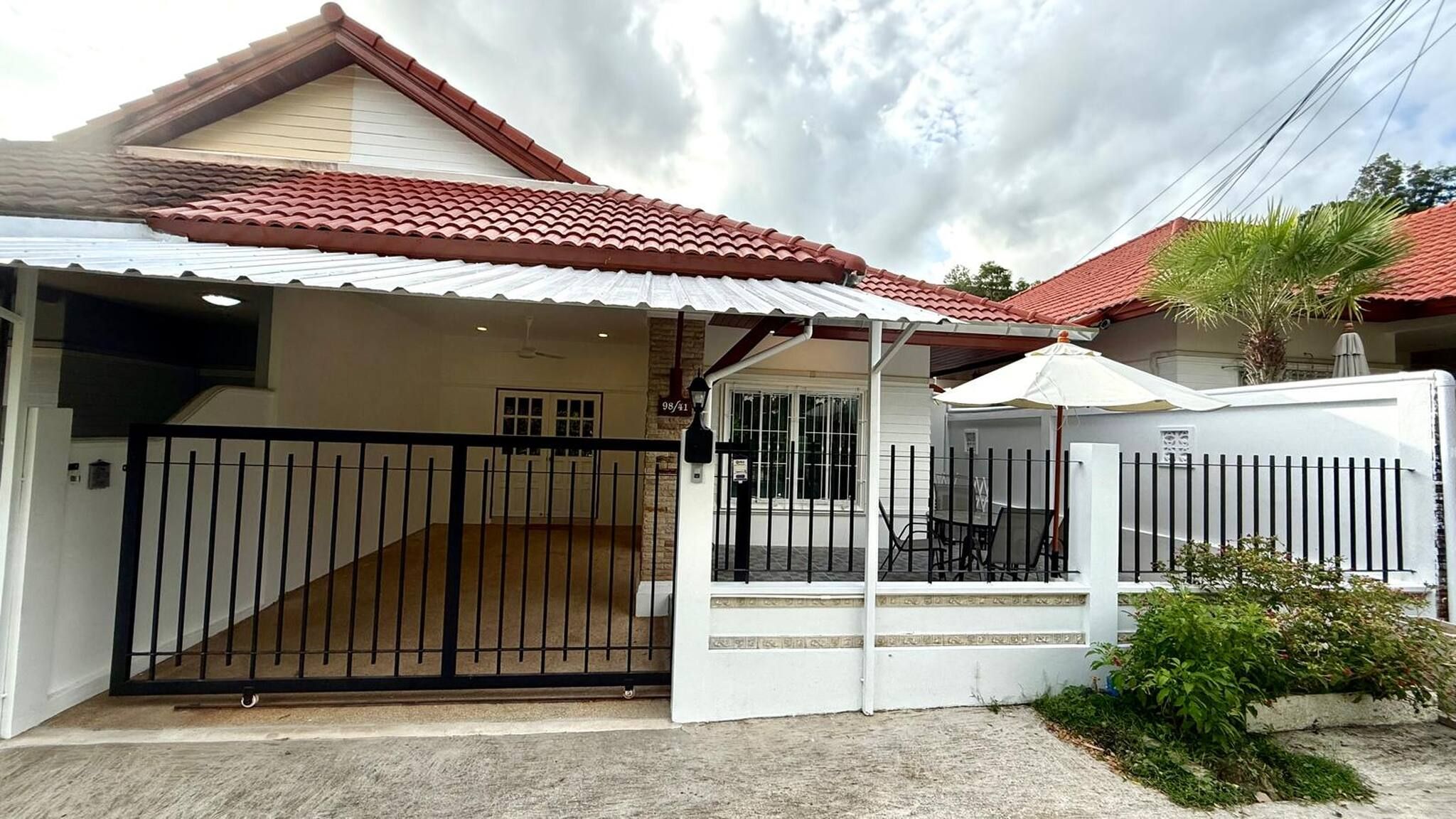 A residential house with a gated entrance, a covered patio area, and a red-tiled roof.