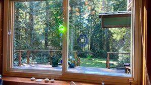 Een kamer met een groot raam met uitzicht op een bebost gebied, een houten terras en een vaste wastafel.