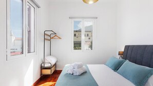 Un dormitorio con cama, lámpara colgante, ventana y estante en la pared.