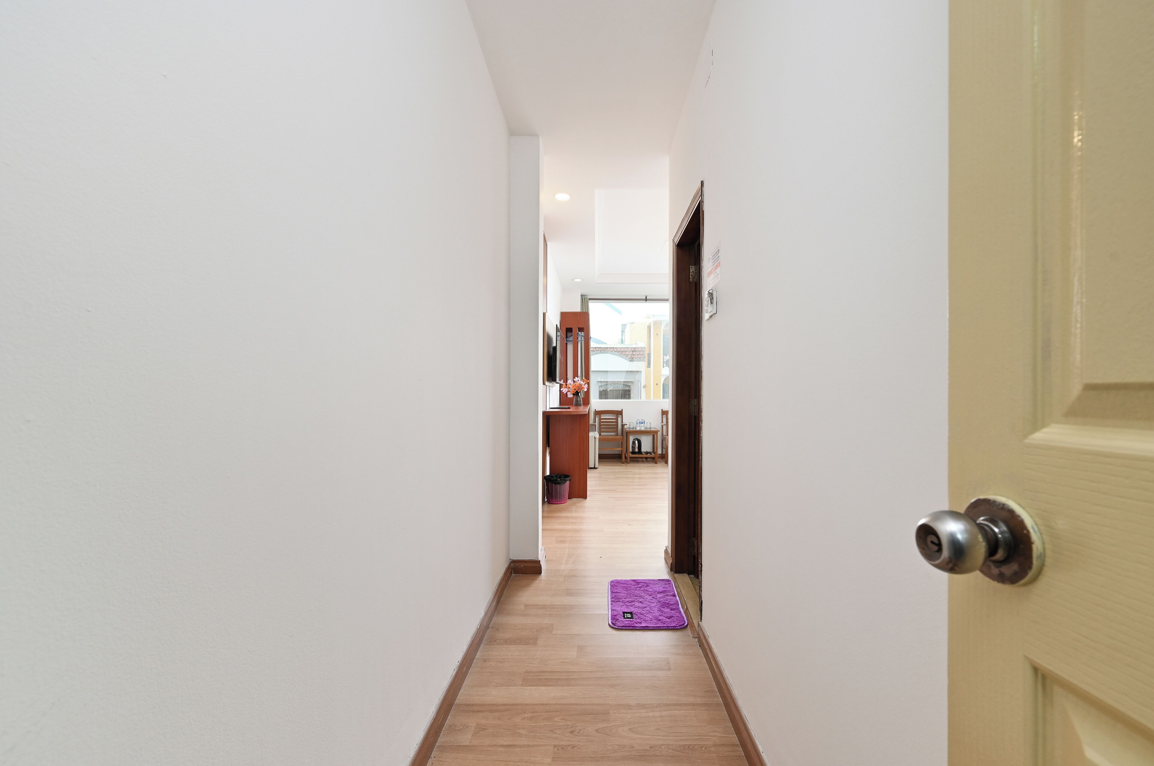 A narrow hallway with a wooden floor leading to a kitchen area.