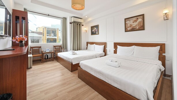 Une chambre d’hôtel avec deux lits, un bureau, une chaise, une fenêtre avec des rideaux et un tableau au mur.