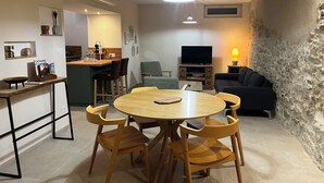 Ein gemütliches Wohnzimmer mit einem runden Holztisch und Stühlen, einem Fernseher und einer Steinwand.