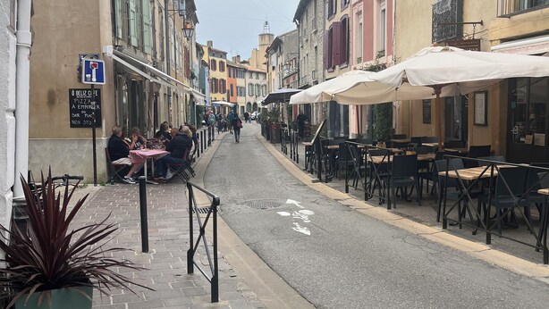 Eine schmale Straße mit Cafés und Restaurants, gepflastert mit Stein und gesäumt von traditionellen Gebäuden.