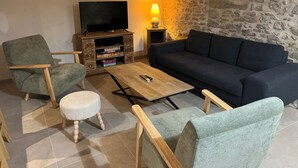Ein Wohnzimmer mit einem dunkelblauen Sofa, zwei Sesseln, einem Holztisch und einem Fernseher auf einer Holzkommode.