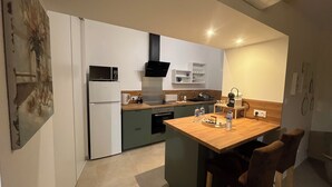 Eine kompakte Küche mit Mikrowelle, Kühlschrank und Kaffeemaschine. Eine Holzinsel mit Barhockerl steht bereit.