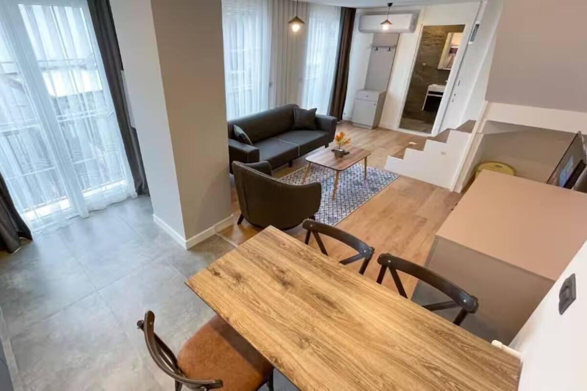Un soggiorno moderno con un tavolo da pranzo in legno, un divano e una scala che conduce a un piano superiore.