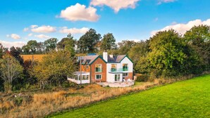 A two-story house with a balcony, surrounded by a grassy field and trees.
