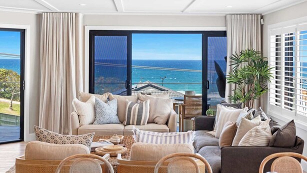 Ein geräumiges Wohnzimmer mit großem Fenster und Blick auf das Meer sowie eine entfernte Küstenlinie.