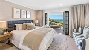 Ein geräumiges Schlafzimmer mit einem großen Bett, einer Sitzecke mit Meerblick und einem Balkon mit Vorhängen.