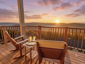 Terraza de madera con dos sillas y una mesa, con vistas a un paisaje pintoresco al atardecer.