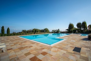 A rectangular swimming pool with a tiled deck, surrounded by greenery and trees. - Suite Panorama Puegnago (Puegnago del Garda)