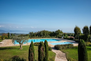 A rectangular swimming pool surrounded by a well-maintained lawn, with a clear view of distant mountains and a clear sky. - Suite Panorama Puegnago (Puegnago del Garda)