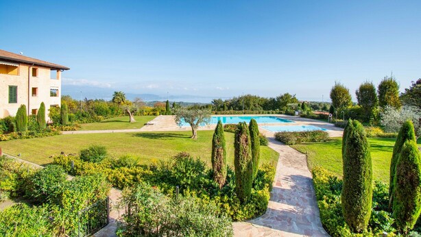 A well-maintained garden with a swimming pool, a pathway, and a building with a tiled roof. - Suite Panorama Puegnago (Puegnago del Garda)
