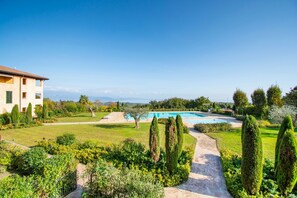 A well-maintained garden with a swimming pool, a pathway, and a building with a tiled roof. - Suite Panorama Puegnago (Puegnago del Garda)