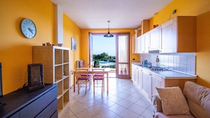 A kitchen with a dining area, a sofa, and a view through the open door. - Suite Panorama Puegnago (Puegnago del Garda)