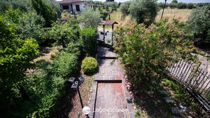 Ein Gartenweg führt zu einem Haus mit einem Steinziegeldach, umgeben von üppiger Bepflanzung und einem eingezäunten Bereich.