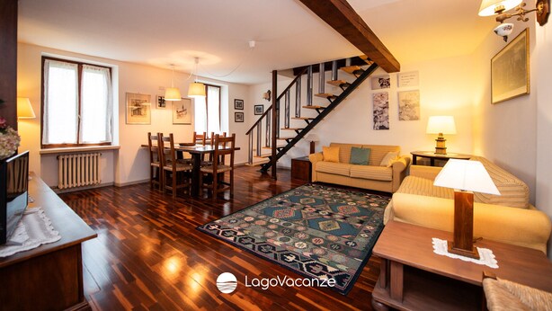 A spacious living room with hardwood flooring, a staircase, a dining area, and a cozy seating area with a lamp. - Casa Reale in Volta Mantovana (Volta Mantovana)