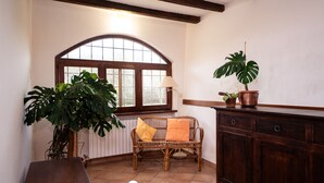 A room with a wooden bench, a wicker sofa with cushions, a large potted plant, a cabinet, and a window with a view. - Casa Reale in Volta Mantovana (Volta Mantovana)