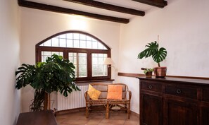 Une pièce comprenant un banc en bois, un canapé en osier avec des coussins, une grande plante en pot, une armoire et une fenêtre donnant sur un beau paysage.