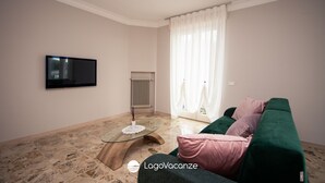 Un salón con sofá verde, una mesa de centro de cristal, un televisor de pantalla plana y un radiador.