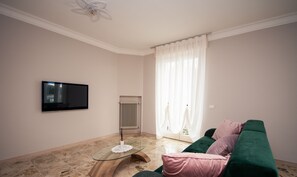 Un salón con sofá verde, una mesa de centro de cristal, un televisor de pantalla plana y un radiador.