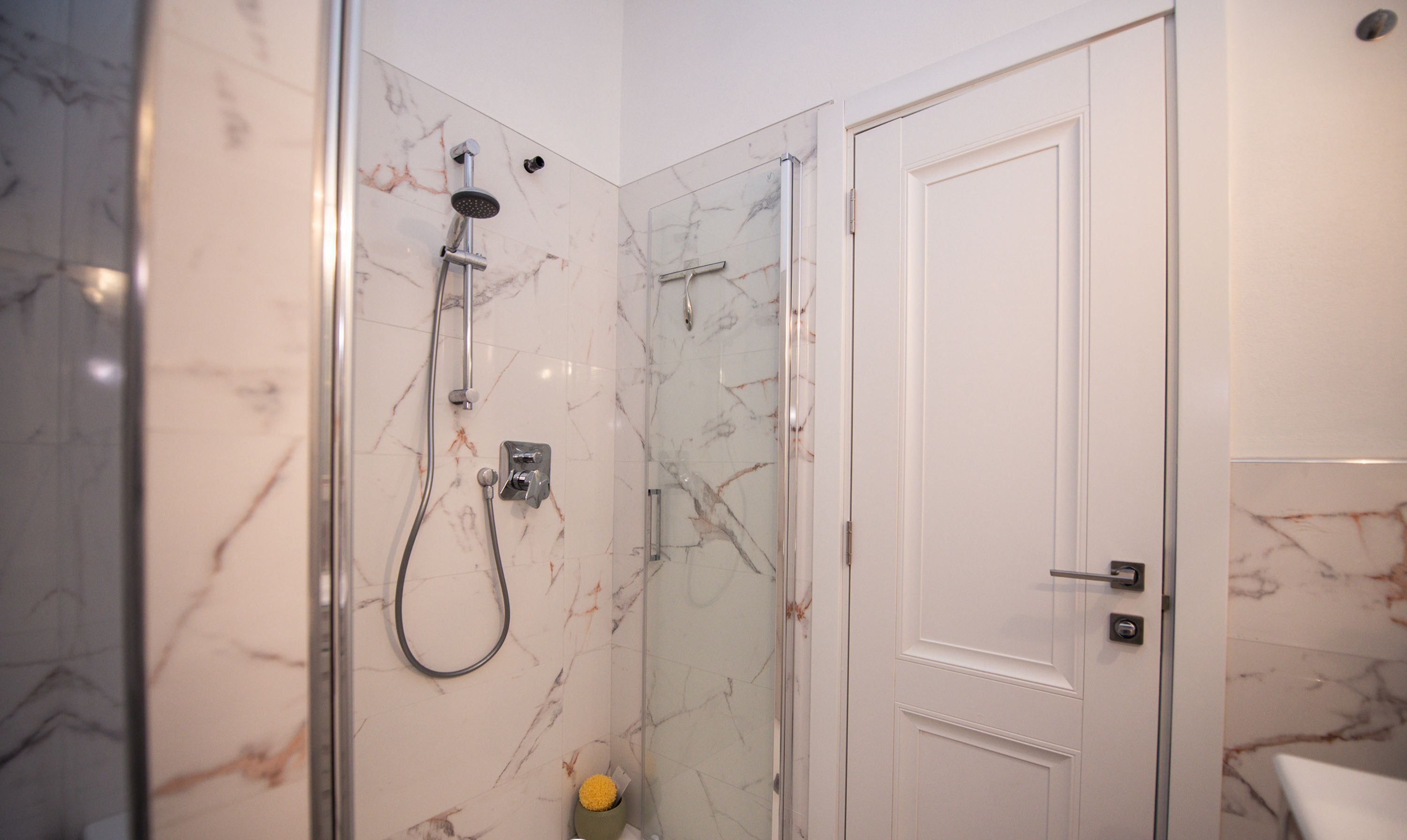 A modern bathroom with a glass-enclosed shower, marble walls, and a white door.