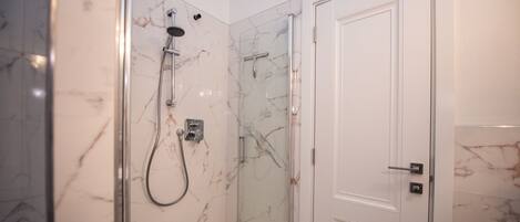 A modern bathroom with a glass-enclosed shower, marble walls, and a white door.