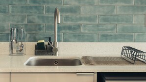 Una cocina con un lavamanos de acero inoxidable, un grifo y un salpicadero de azulejos color turquesa.