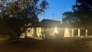 A house with a cross on the roof, surrounded by trees and illuminated by lights.