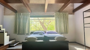 A bedroom with a bed, a window with curtains, a staircase, and a view of trees outside.