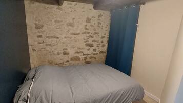 Una habitación pequeña y rústica con una cama individual, un muro de piedra y techo de madera.