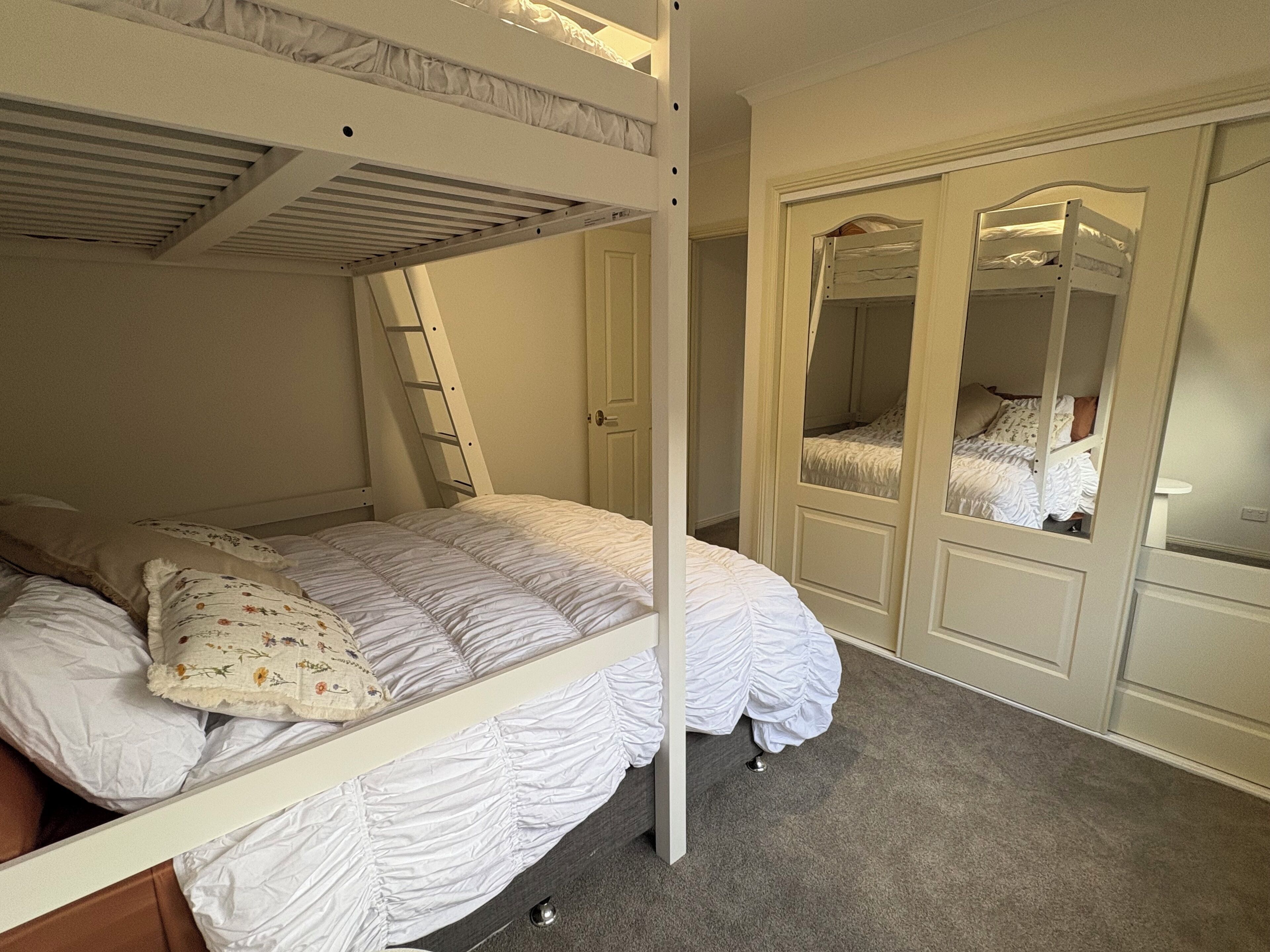 A bunk bed with a ladder, a wardrobe with a mirror, and a door leading to another room.