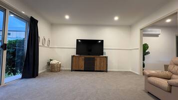 A living room with a flat-screen TV on a wooden stand, carpeted floor, and a beige sofa.